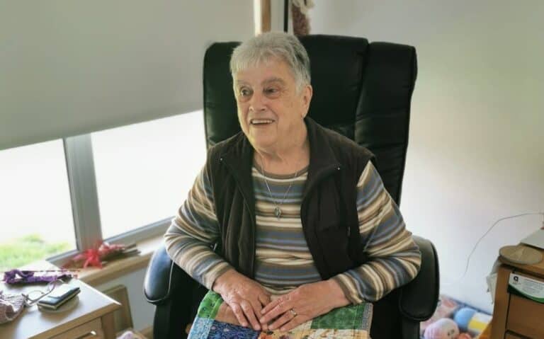 A grey haired woman sits in a chair in her new home