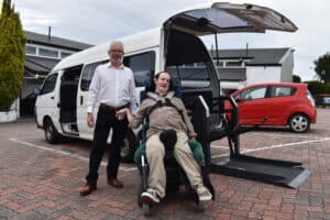 man in shirt and a man in a wheelchair stand in front of a wheelchair accessible van