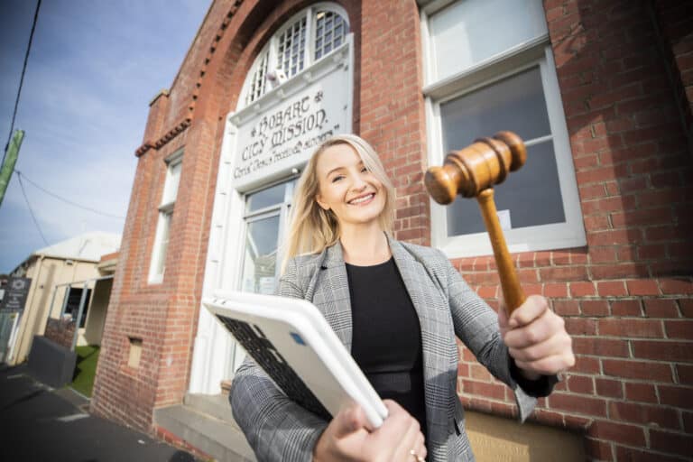 blonde haired woman holding a gavel in front of a brick building