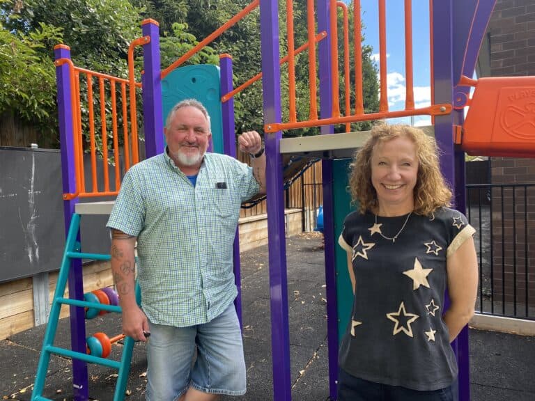man and women standing in front of colourful playground smiling at the camera