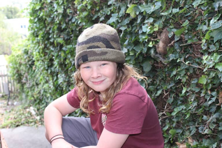 boy in beanie smiling in front of a green garden background